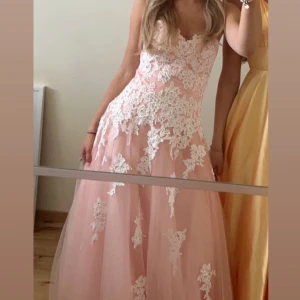 Rosa balklänning med spetsdetaljer - As snygg ljusrosa balklänning med diamanter. Axelbandslös och justerbar vid ryggen. Passar mig som har storlek XS/S perfekt men den passar en mindre eller en större storlek också pågrund av snörningen på ryggen. Använd en gång. Lånade bilder. 