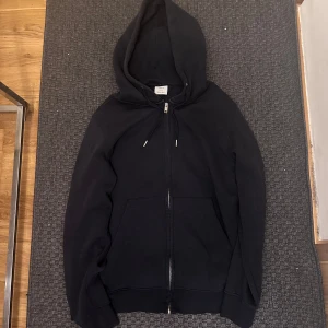 Mango Zip Hoodie - Säljer en mörkblå hoodie från MNG i storlek L. Tröjan har dragkedja framtill, huva med snören och två fickor. Perfekt för en avslappnad stil och enkel att matcha med det mesta.