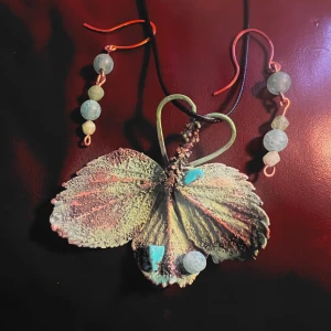 Halsband och örhängen med blad och stenar - Unikt halsband med stort bladformat hänge i grönt och turkost, dekorerat med pärlliknande stenar. Matchande örhängen med gröna pärlor och kopparfärgade detaljer. Perfekt för dig som gillar naturinspirerade smycken.