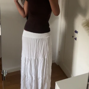 Vit långkjol med resårmidja - Säljer en vit långkjol med bred resår i midjan. Kjolen är luftig och har ett lätt skrynklat tyg som ger en avslappnad känsla. Perfekt för varma dagar och enkel att matcha med olika toppar.