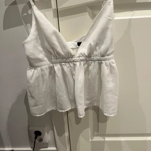 Vit linne från BikBok - Säljer en söt vit linnetopp från BikBok med smala axelband och v-ringning. Toppen har en lätt rynkad midja som ger en luftig och somrig känsla. Perfekt till varma dagar eller att styla lager på lager.