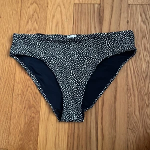 Svart bikiniunderdel med vitt prickigt mönster - Säljer en svart bikiniunderdel med vitt prickigt mönster. Klassisk modell med normal passform och fodrad insida. Perfekt för stranden eller poolen.