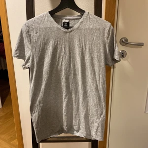 Grå v-ringad t-shirt från 157 - En enkel och stilren grå t-shirt från 157 med v-ringad hals. T-shirten är kortärmad och har en normal passform. Perfekt basplagg i mjuk bomull som funkar till det mesta.