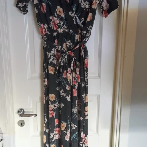 Blommig byxdress från NLY Trend - Säljer en svart byxdress med blommigt mönster från NLY Trend i storlek XS. Klänningen har korta ärmar, omlottliv och knytband i midjan. Tillverkad i mjuk polyester, perfekt för sommarens tillfällen. Den är använd en gång. Men den har ytludd som den fick direkt 
