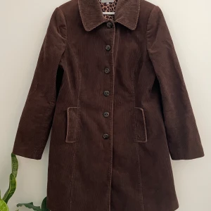 Brun manchesterkappa från Per Una - Säljer en brun kappa i manchester från Per Una med klassisk krage och knappar framtill. Fodret har ett prickigt mönster i brunt och beige🌷 Stängs med knappar och har två ytterfickor. Storlek M-XL beroende på önskad passform. Nytvättad och i fint skick!  Axelbredd: cirka 40cm Bredd från armhåla till armhåla: 50cm Ärmlängd från armhåla: 43cm Längd från axel till botten: 89cm