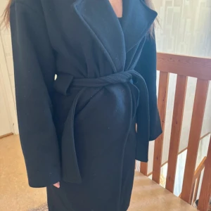 Svart kappa från Vero Moda med bälte - Säljer en svart kappa från Vero Moda i storlek L. Kappan har ett brett bälte i midjan, stora slag och långa ärmar. Perfekt för kyligare dagar och har en klassisk, stilren look.