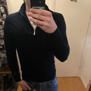 Svart stickad tröja med dragkedja från Bruun & Stengade - Säljer en svart stickad tröja från Bruun & Stengade i storlek S. Tröjan har hög krage och dragkedja vid halsen, perfekt för lager-på-lager. Snygg och enkel design som passar till jeans eller chinos.