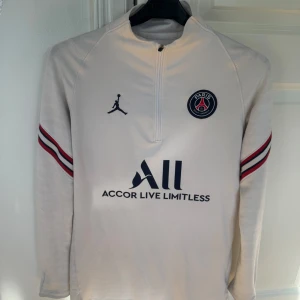 Vit långärmad PSG tröja  - Säljer en vit långärmad Paris Saint-Germain fotbollströja från Jordan med svarta och röda detaljer. Tröjan har dragkedja vid halsen, PSG-logga på bröstet och texten 'Accor Live Limitless' samt 'Visit Rwanda' på ryggen. Köpt på Unisport. I dam storlek xs 