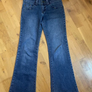 Lee Pipes bootcut jeans i blå denim - Säljer ett par klassiska blå bootcut jeans från Lee Pipes med fem fickor och snygga detaljer på bakfickorna. Jeansen har låg midja och är tillverkade i slitstark denim. Perfekta för dig som gillar retrostil och bredare ben.