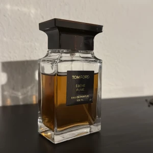 Tom Ford Ébène Fumé Eau de Parfum 100 ml - Lyxig parfym från Tom Ford i en elegant, fyrkantig glasflaska med mörkbrunt lock. Doften Ébène Fumé är känd för sina rökiga och träiga toner. Flaskan rymmer 100 ml och har en exklusiv känsla. Har ca 80% kvarstående