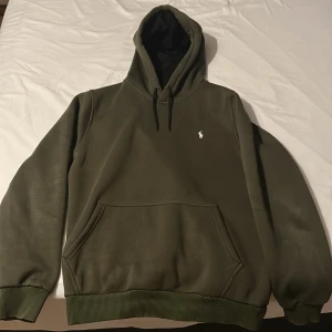 Olivgrön hoodie från Ralph Lauren - Säljer en olivgrön hoodie från Ralph Lauren med klassisk broderad logga på bröstet. Tröjan har huva med dragsko och en stor magficka. Perfekt för en avslappnad stil.