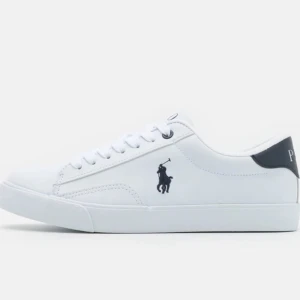 Vita sneakers från Polo Ralph Lauren - Snygga vita sneakers från Polo Ralph Lauren med klassisk logga i mörkblått på sidan och mörkblå detalj vid hälen. Passar som storlek 37. Köpta för 979kr på Zalando