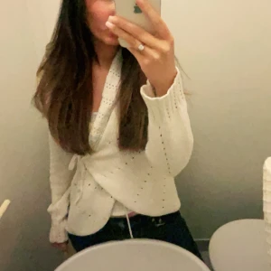  Söt Vit omlott kofta med kny - Säljer en vit omlott kofta med knyt i midjan. Koftan har lång ärm och är stickad med små hålmönster för en extra detalj. Perfekt för lager-på-lager och passar till mycket.