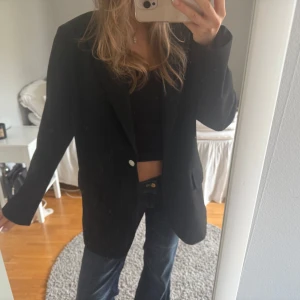 Svart  oversized kavaj - Säljer en svart kavaj med oversized passform och långa ärmar. Kavajen har en enkel knäppning framtill och klassisk krage. Perfekt att styla till jeans eller kjol för en stilren look. 