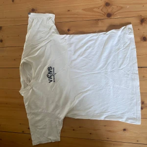 Vit t-shirt från Vans med tryck - Vit t-shirt från Vans med tryck på bröstet och stort motiv på ryggen med texten 'Together it's time to love the earth and embrace it from the core'. Skön passform och tillverkad i bomull. Perfekt för dig som gillar streetwear och vill ha ett statement-plagg.