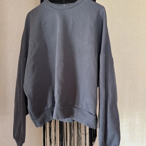 Grå sweatshirt från Nelly - En enkel och stilren grå sweatshirt från Nelly. Tröjan har rund halsringning, långa ärmar och ribbade muddar vid ärmslut och nederkant. Perfekt för en avslappnad och bekväm stil.