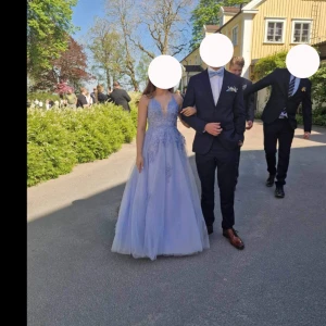 Ljusblå balklänning med spetsdetaljer - Säljer en ljusblå långklänning med v-ringning och tunna axelband. Klänningen har vackra spetsapplikationer och snörning i ryggen. Kjolen är i flera lager tyll för en extra volym. Den är uppsydd till mig som är 156 och har som klackar som är ca 10 cm höga🩵. Köptes ny förra året:)