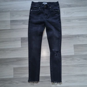 Svarta skinny jeans från Denim by Skill - Snygga svarta skinny jeans från Denim by Skill i storlek 146. Jeansen har slitningar på ena benet och råa, fransiga benslut för en cool look. Klassisk femficksmodell med dragkedja och knapp. Perfekta för dig som gillar streetstyle.