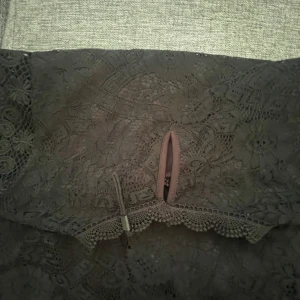 Svart spetsklänning med hög krage - Supersnygg svart kortklänning från H&M i spets med blommigt mönster. Hög krage, ärmlös design och fina volangdetaljer vid axlarna. Perfekt för dig som vill sticka ut med en elegant och trendig look.