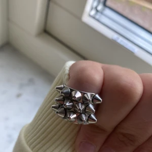 Edblad ring - Unik silvrig ring dekorerad med flera små nitar som ger ett edgy och modernt utseende. Perfekt för att ge din outfit en tuff touch. Ringen har en bred design och är tillverkad i metall.