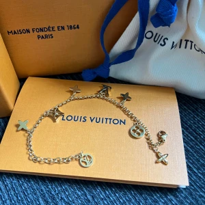 Louis Vuitton guldigt armband med berlocker - Superfint armband från Louis Vuitton i guldtonad metall med flera ikoniska LV-berlocker och blommor. Kedjan är tunn och smidig, och berlockerna har både logga och klassiska former. Kommer med originalask, påse och kvitto.