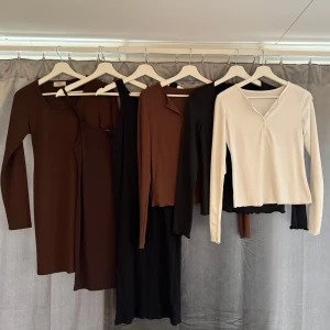 Klädpaket  - 6 plagg. 3 st långärmade topp/t-shirt med knappar framtill (vit, brun & svart). 3 st klännigar, 2 korta (bruna) 1 medel lång (svart) . Allt i fint skick, eller bättre. Lapparna i plaggen säger lite olika storlekar med skulle säga att allt passar en S/M. Lite olika märken, bland annat Chiquelle och 157. Katt finns i hemmet