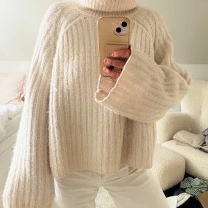 Beige ribbstickad polotröja - Supermysig beige polotröja med breda, ribbstickade ränder och oversized passform. Tröjan har långa ärmar och hög polokrage, perfekt för lager på lager. Materialet känns fluffigt och mjukt, vilket gör den extra skön under kyliga dagar.