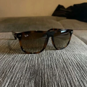 Bruna Wayfarer-solglasögon Ray-Ban - Snygga Wayfarer-solglasögon från Ray-Ban med brunmelerad båge och mörka glas. Klassisk fyrkantig form och diskret logga på båda sidor. Perfekt accessoar för att lyfta din stil i sommar.