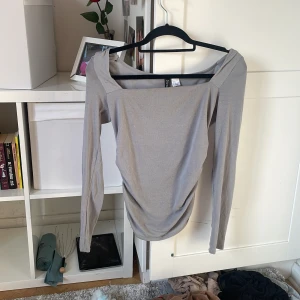 Grå långärmad offshoulder topp - Säljer en stilren grå långärmad topp från Chiquelle med offshoulder-skärning och lätt rynkade detaljer framtill. Toppens material är mjukt och stretchigt, perfekt för en trendig och avslappnad look. Passar dig som gillar minimalistisk stil med en twist.