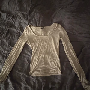 Beige långärmad topp med rund hals - En enkel och stilren beige långärmad topp med rundad halsringning. Perfekt att styla med jeans eller kjol för en clean look. Tunn och mjuk i materialet, sitter snyggt och följsamt på kroppen.