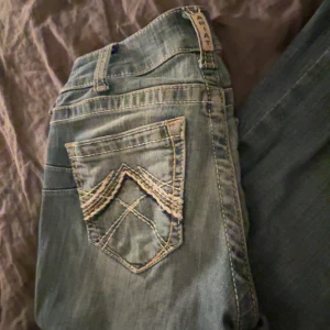  Low waist Ariat REAL bootcut jeans ljusblå 25R - Säljer ett par ljusblå bootcut jeans från Ariat REAL med snygga kontrastsömmar och broderad bakficka. Jeansen har paisleymönstrat innerfoder i midjan och klassisk femficksdesign. Perfekta för dig som gillar western-inspirerad stil.