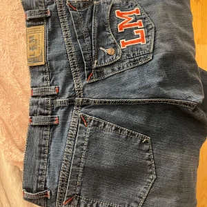 Blå bootcut jeans med broderi från L&M - Säljer ett par blå bootcut jeans från L&M med coola röda och vita broderade detaljer på fickorna. Storlek står inte men passar mig som har 36-38 i jeans. 