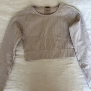 Beige ribbad croppad topp Aim'n - Säljer en beige croppad långärmad topp från Aim'n. Toppen är ribbad och har en tight passform med rund halsringning. Perfekt för dig som gillar stilrena och bekväma plagg till träning eller chill. Metallogo bak i nederkant för extra detalj.