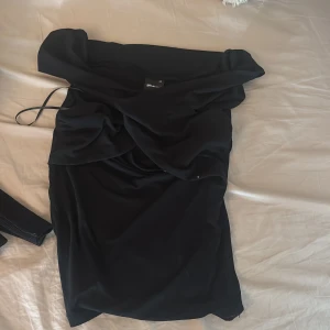Svart offshoulder klänning Gina Tricot - Säljer en svart kortklänning från Gina Tricot i storlek XS. Klänningen har en snygg offshoulder-design och är figurnära med en draperad överdel. Perfekt för dig som vill ha en stilren och trendig look.