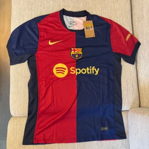 FC Barcelona matchtröja Nike röd/blå - Snygg FC Barcelona fotbollströja från Nike med klassisk röd och blå halvdelad design. Tröjan har klubbmärke, Nike-logga och sponsorer i gult framtill. Tillverkad i lätt och ventilerande polyester, perfekt för match eller träning.