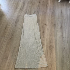 Ljusgrå långklänning Gina Tricot - Supersnygg ljusgrå långklänning från Gina Tricot. Klänningen har smala axelband och en enkel, rak passform som faller snyggt längs kroppen. 