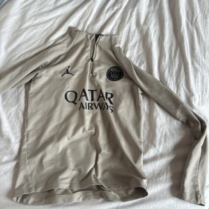 Beige PSG x Jordan långärmad tröja - Strl XS - Snygg beige långärmad fotbollströja från PSG x Jordan med svart Paris Saint-Germain-logga, Jordan-logga och Qatar Airways-tryck på bröstet. Halv dragkedja framtill och svart signaturdetalj på ärmen. Slim fit-modell i mjukt, stretchigt material.