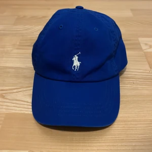 Blå keps från Polo Ralph Lauren - Snygg blå keps från Polo Ralph Lauren med klassisk broderad logga framtill och justerbart spänne bak. Jag har bara använt den en gång och är i nyskick. Kepsen är köptes från johnells och är äkta. Perfekt för sommaren. Hör av er vid funderingar ✌️