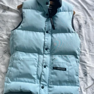 Ljusblå dunväst från Canada Goose - Blå Canada Goose-väst i fint skick. Supervarm och snygg perfekt till hösten eller som lager under jacka på vintern. Klassisk modell med bra passform. Säljer bara för att den tyvärr blivit för liten. Nypris ca 5000, men jag har ärvt den och därav har jag inte original förpackning samt äkthetsbevis.   Strl S.