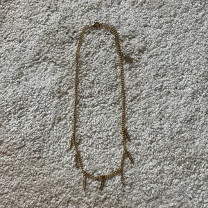 Guldigt halsband med spetsiga hängen - Snyggt guldigt halsband med flera små spetsiga hängen som har glittrande stenar. Kedjan är tunn och smidig, perfekt för att ge en cool touch till din outfit. Hängena är dekorerade med små stenar som ger extra bling. OBS!!! KOMMER GÖRAS RENT INNAN SICKAD