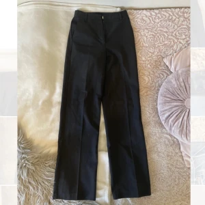 Svarta kostymbyxor från BikBok - Klassiska svarta kostymbyxor från BikBok i rak modell med hög midja. Byxorna har hällor för bälte, diskreta sidfickor och stängs med dragkedja och knapp. Perfekta till en snygg och clean look.