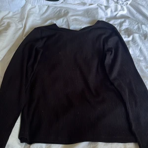 Svart ribbad långärmad tröja Lindex - Svart långärmad tröja från Lindex med ribbad struktur och snygg detalj med korsade band i halsringningen. Perfekt basic med en twist, passar till allt och är superenkel att styla. Mjuk och skön, i stretchigt material.