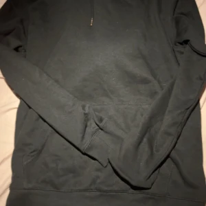 Svart hoodie från 157 med huva - Svart hoodie från 157 i storlek M. Klassisk modell med huva och snörning, samt en stor magficka framtill. Tillverkad i mjuk bomullsmix som är skön att ha på sig. Perfekt för chill dagar eller när du vill ha en enkel och stilren look.