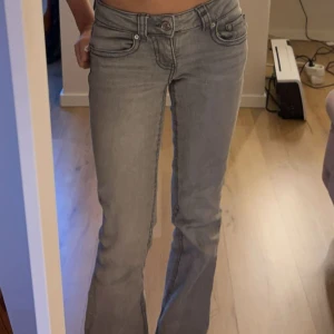 Grå bootcut jeans med låg midja - Säljer ett par grå jeans med snygg bootcut och låg midja. Jeansen har klassiska fem fickor, markerade sömmar och stängs med knapp och dragkedja. Perfekta för dig som gillar en avslappnad men trendig look.
