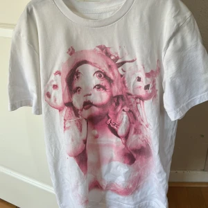 Melanie Martinez Portals tour t-shirt - Vit t-shirt från Melanie Martinez Portals tour med rosa tryck fram och bak. Framsidan har ett konstnärligt motiv i rosa toner och baksidan har turnédatum och PORTALS-tryck. Gjord i 100% ekologisk bomull och har klassisk passform med rund hals och korta ärmar.