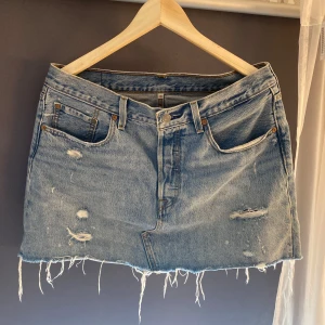 Levi's ljusblå jeanskjol med slitningar - Ljusblå jeanskjol från Levi's med rå kant och slitna detaljer framtill och baktill. Kjolen har används fåtal gånger och har inga skador. 