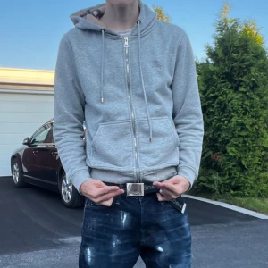 Grå Burberry hoodie med dragkedja - Snygg grå hoodie från Burberry med klassiskt rutigt foder i huvan. Tröjan har dragkedja framtill, snörning i huvan och två fickor. Perfekt för dig som gillar stilren streetwear med en touch av lyx.