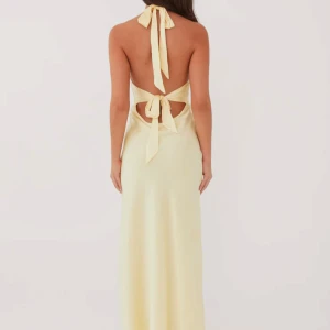 Ljusgul satin klänning  - Snygg ljusgul långklänning i satinliknande material med djup v-ringning och öppen rygg. Klänningen har breda band som knyts i nacken och i ryggen för en cool och elegant look. Perfekt för sommarens alla tillfällen. Änvänf endast en gång och tvättad en gång, inga tecken på användning. 
