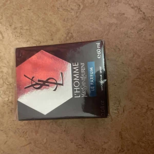 YSL L'Homme Le Parfum 60ml - YSL L'Homme Le Parfum, 60 ml, i en snygg fyrkantig kartong med metallicröd, silver och svart design samt YSL-logga. Parfymen är en eau de parfum för män och kommer i en stilren förpackning som känns lyxig och modern.
