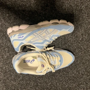 ASICS sneakers i ljusblått och beige - Snygga ASICS sneakers i en fräsch kombo av ljusblått och beige med mesh och mockadetaljer. Skorna har en chunky sula, klassisk snörning och lila ASICS-logga. Perfekta för dig som gillar sportig stil med retrovibbar.